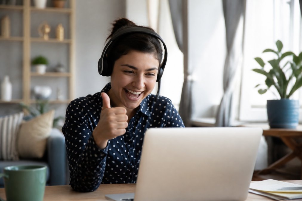 Remote employees on a video call smiling and reacting positively to a message on screen, with one person giving a thumbs up gesture in appreciation
