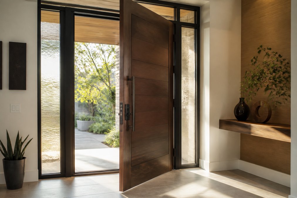 An elegant open luxury entry door in a modern home foyer showing detailed architectural hardware, natural light streaming through sidelites, and premium materials with rich wood grain finish