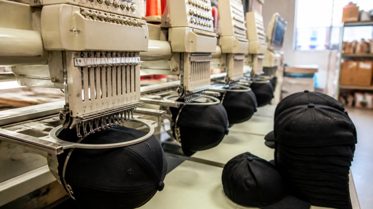 Commercial embroidery machine stitching a logo onto navy embroidered hats in a production workshop