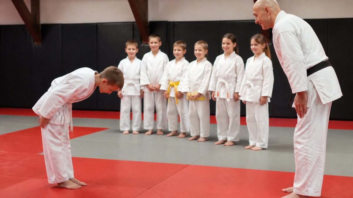 A young student bowing to an instructor within a supportive martial arts community dojo setting.