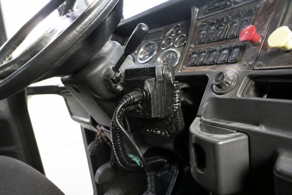 Close-up view of a commercial truck's dashboard and cab interior, showing the location of electronic data recorders and monitoring equipment mounted on the steering column and dashboard