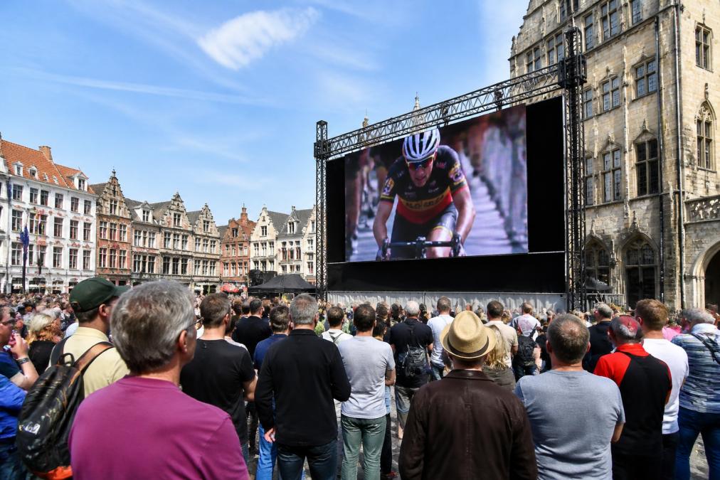 Een groot LED-scherm op een drukbezocht buitenevenement in een Belgische stad, met bezoekers die naar het scherm kijken tijdens een live uitzending