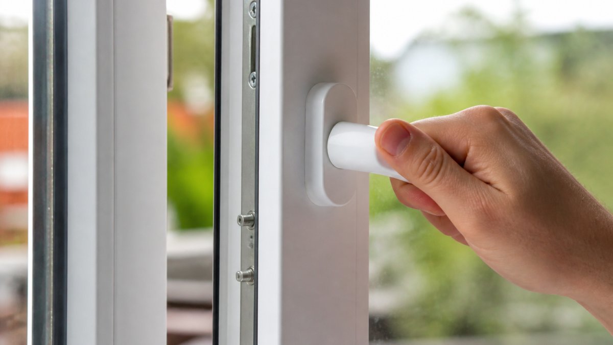 Hand turning a uPVC window handle to inspect the mechanism of faulty window locks on the frame edge