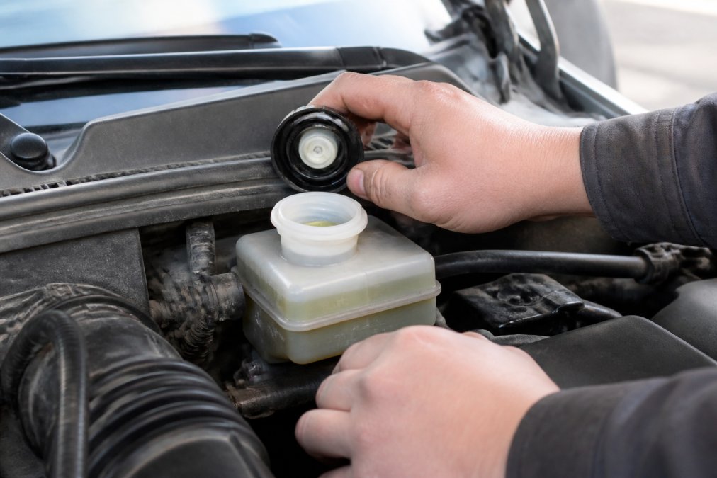 Mechanic checking a brake fluid reservoir to identify low brake fluid signs via visible level markings