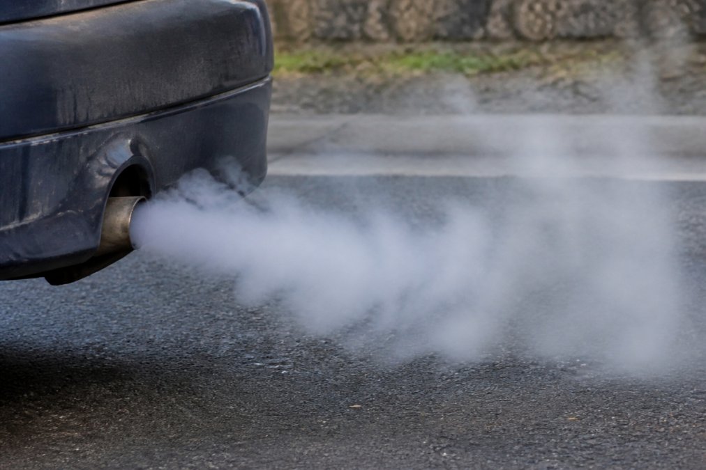 White smoke billowing visibly from a vehicle's tailpipe during engine idle, showing distinctive vapor clouds against the background