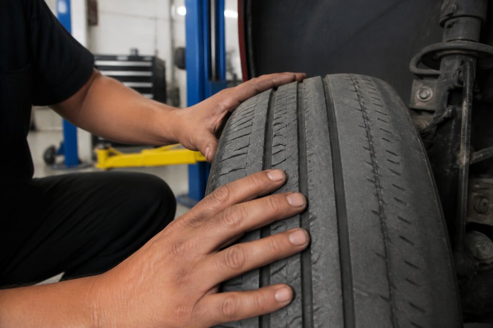 Technician inspecting uneven inner tire tread wear caused by poor wheel alignment