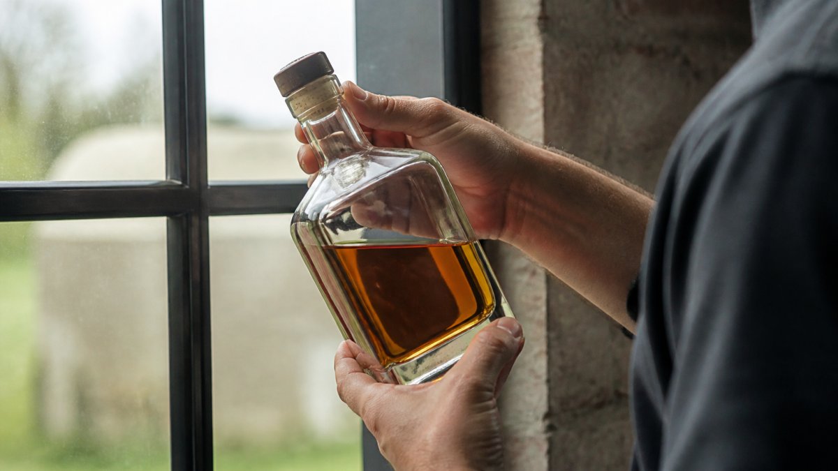 Hands holding a whiskey finished bottle up to natural light to inspect the fill level and cap seal.