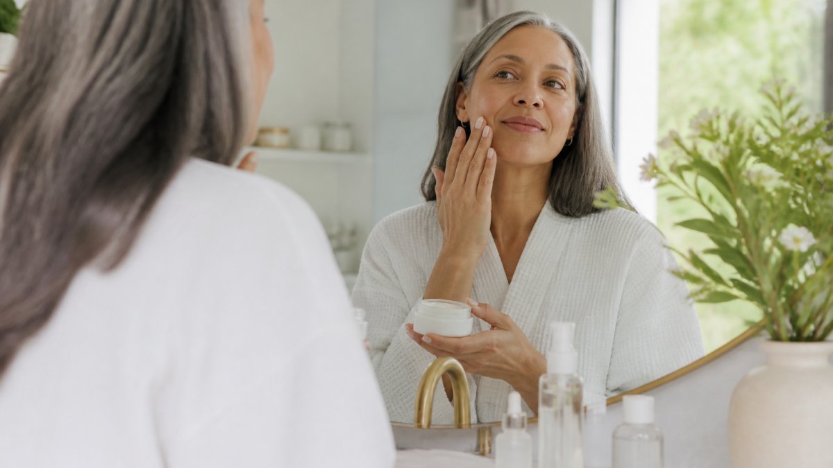 A woman with sensitive skin gently applying a fragrance-free moisturizer in a calm, softly lit bathroom, with a simple skincare routine laid out on the counter