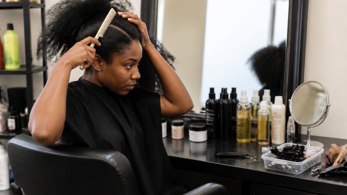 Woman sectioning natural hair with a comb before her professional braiding appointment in a bright salon