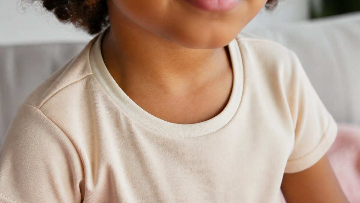 Close-up of a young child wearing a soft organic cotton t-shirt, showing smooth flat seams at the shoulders and sleeves with focus on the neck area where the self-fabric tape is visible inside, natural indoor lighting