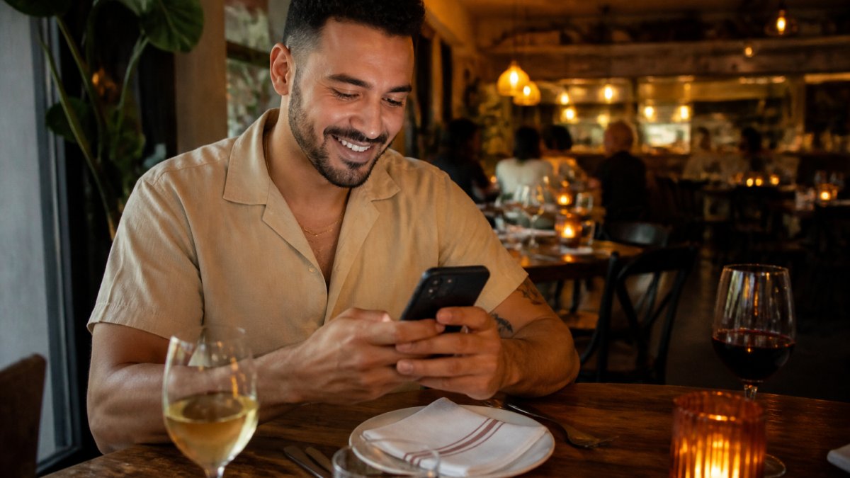 Person smiling while using smartphone to book a reservation, with warm restaurant lighting softly visible in the background