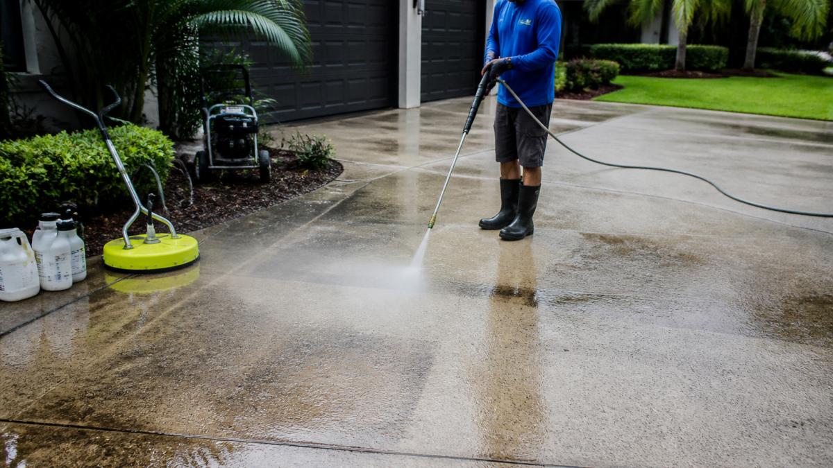 Professional demonstrating power washer technique on concrete driveway surface, removing visible dirt and grime with controlled spray pattern