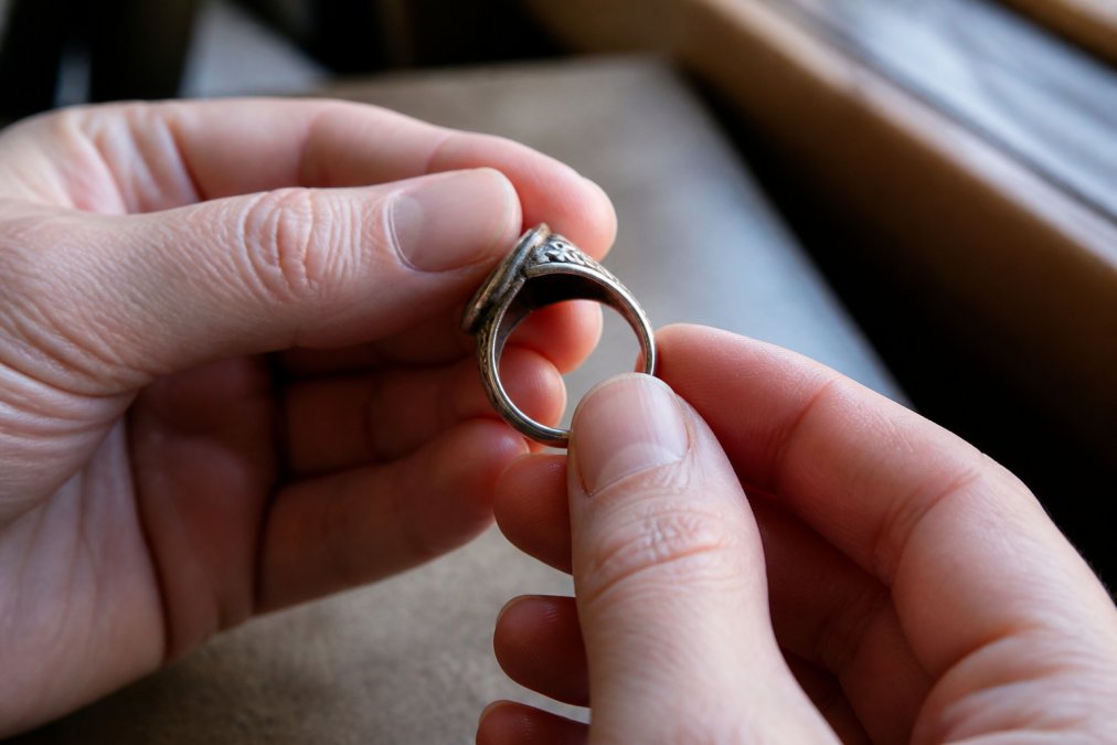 Close-up of a person's hands holding an antique silver ring in soft window light, showing natural patina and smooth wear patterns on the band edges