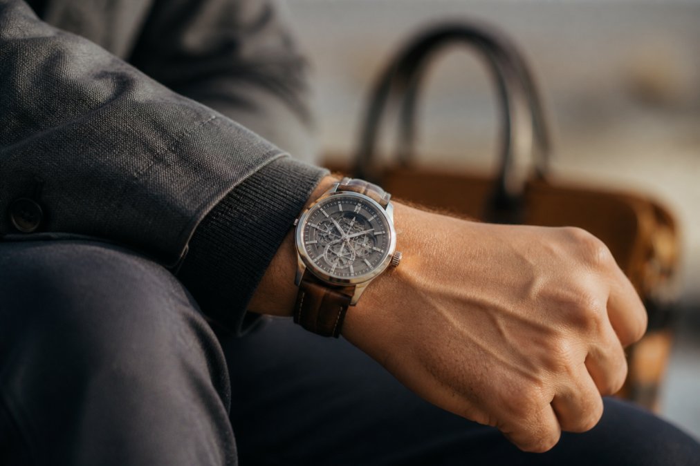 Man's wrist wearing a handcrafted watch with visible leather strap and detailed dial, soft natural daylight highlighting the quality craftsmanship and engraved details