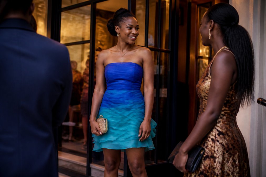 Woman wearing a vibrant blue ombré organza mini dress at an evening cocktail event, styled with delicate gold jewelry and strappy heels, standing in soft warm lighting near a venue entrance