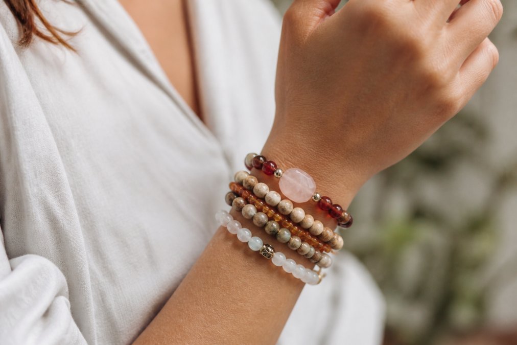Close-up of a woman wearing a stack of earthy handmade jewellery bracelets made from polished semi-precious stones.
