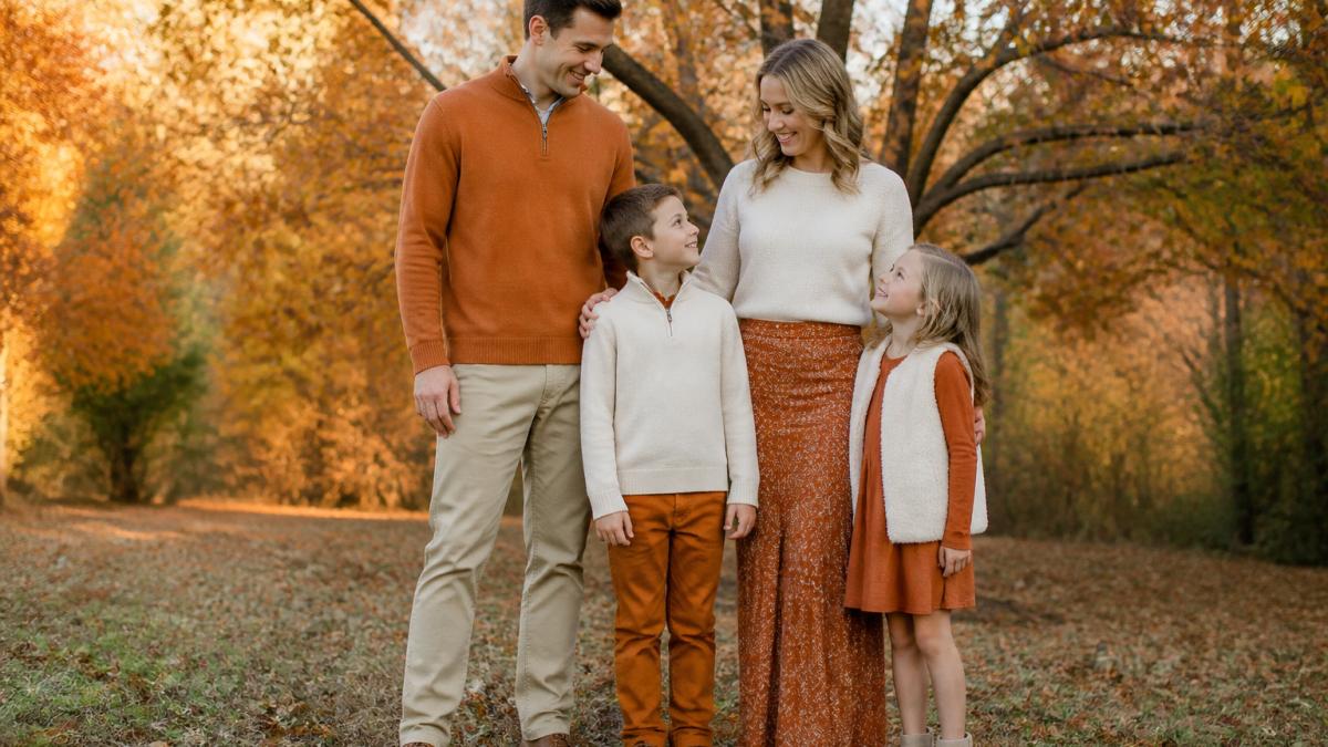 Family of four wearing coordinated burnt orange and cream outfits standing in a sunny autumn park