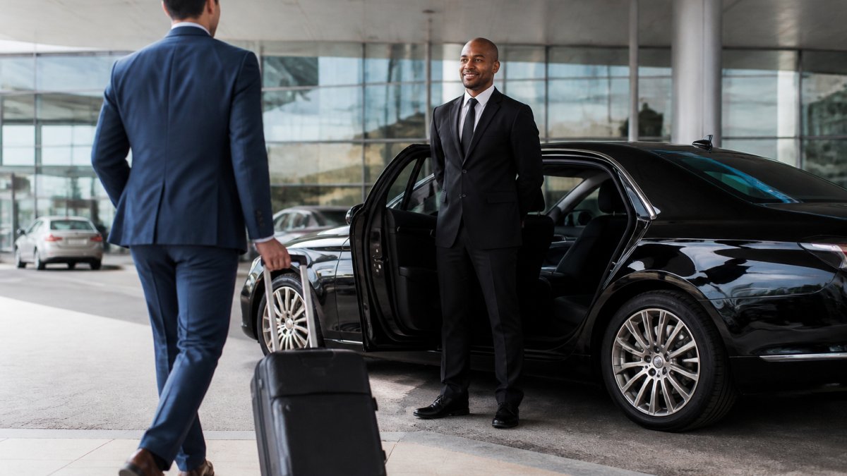 Chauffeur in a suit waits by a luxury sedan to help a traveler avoid airport stress with private ground transport.