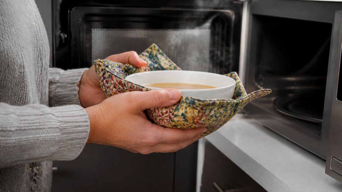 Hands wearing a colorful cotton bowl cozy to safely hold a hot bowl fresh from the microwave