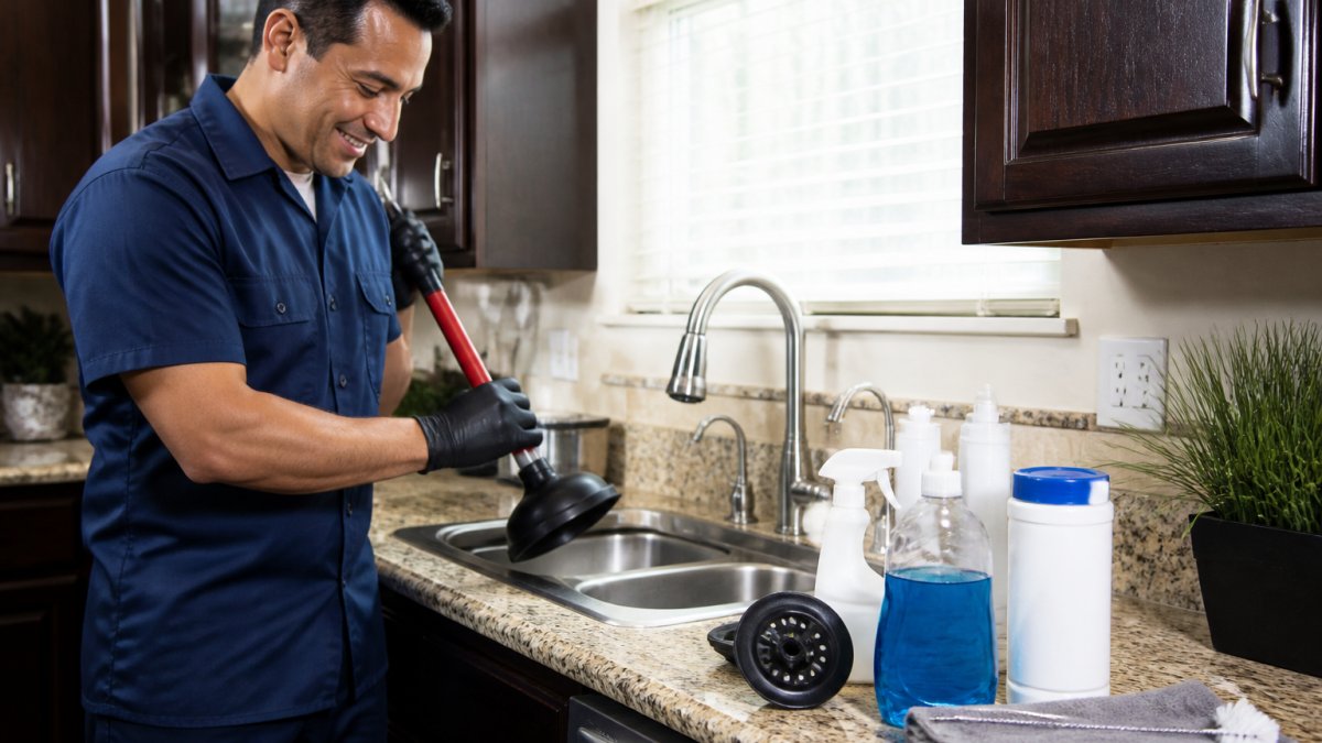Homeowner using a plunger and drain strainer to prevent recurring drain clogs in a kitchen sink