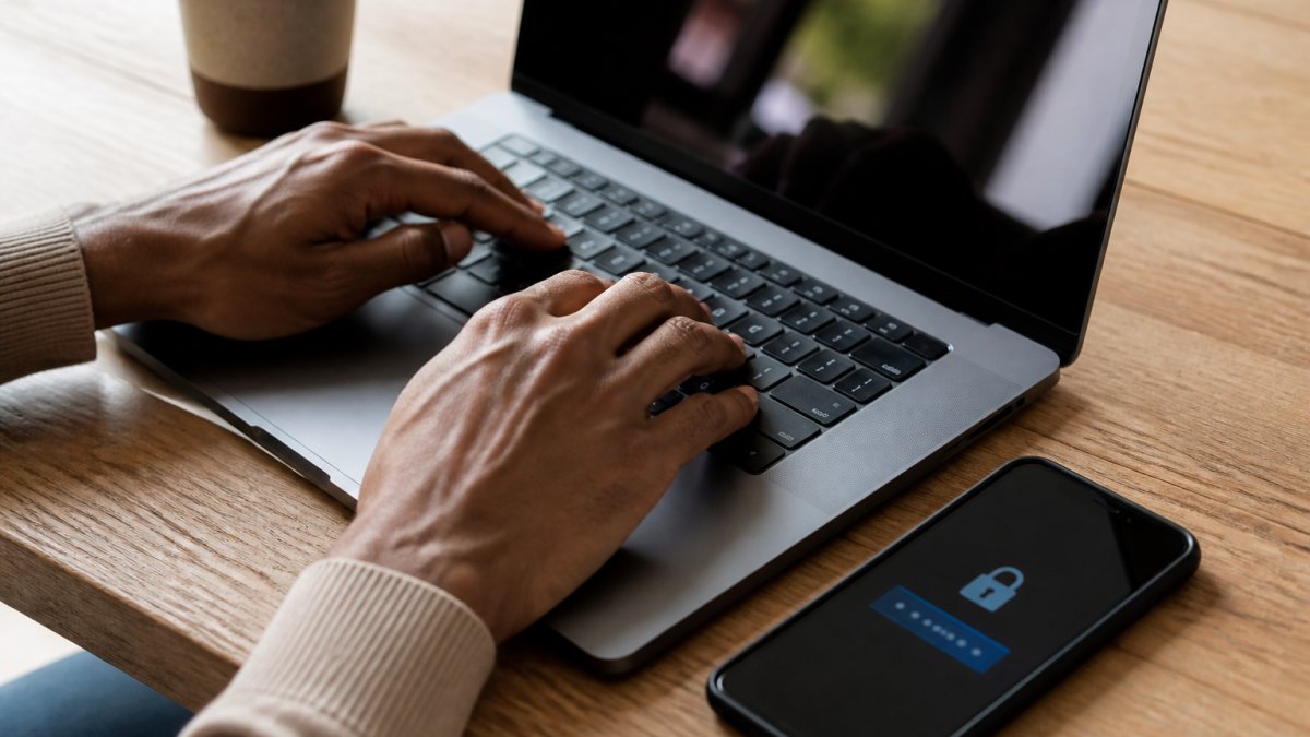 Close-up of hands typing a secure password on a laptop keyboard, with a smartphone displaying a two-factor authentication code notification nearby