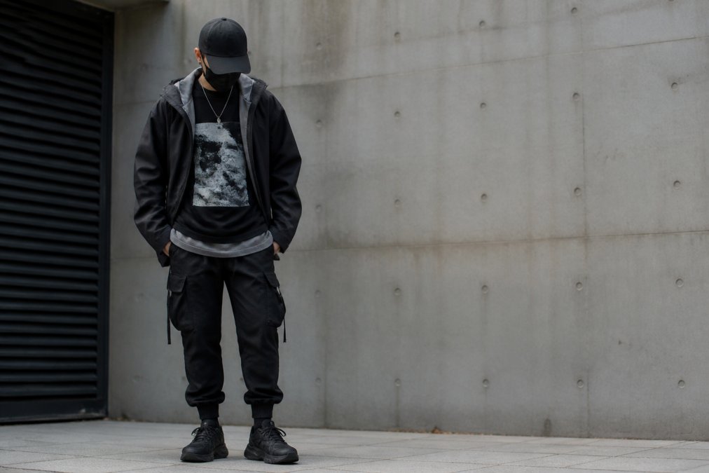 Person wearing a layered techwear outfit with a heavyweight graphic tee under an oversized jacket with drop shoulders, showing how pieces stack visually and functionally with tapered cargo pants