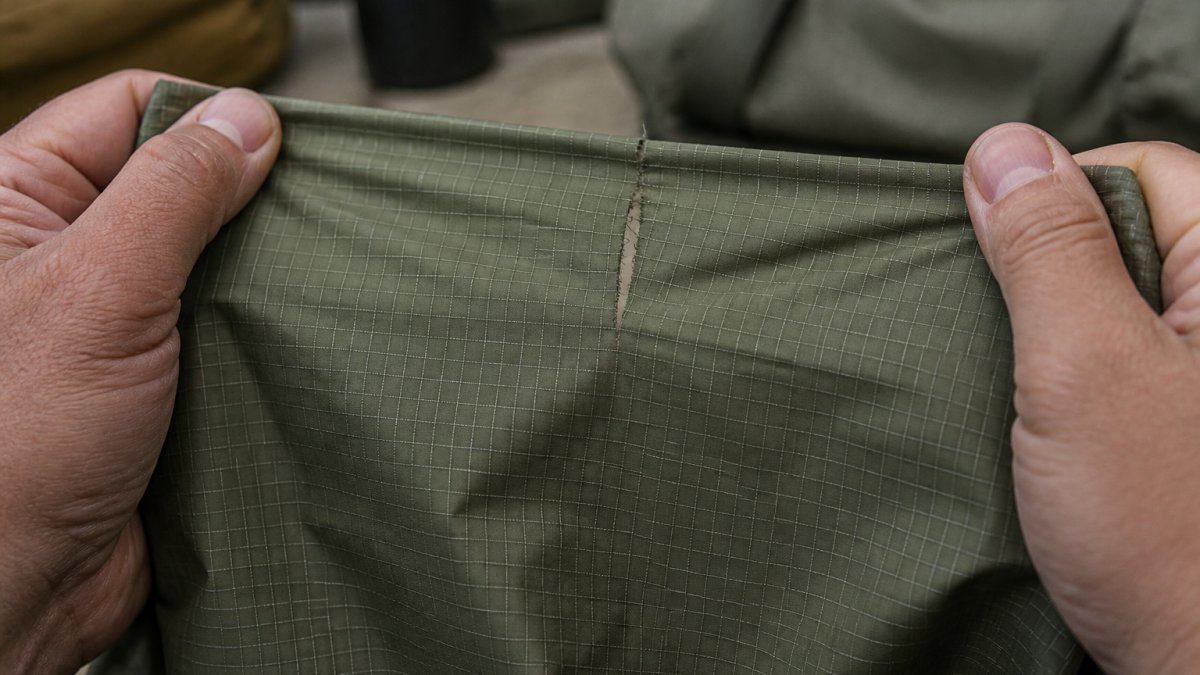 Hands pulling ripstop fabric taut during a tear resistance test where the grid pattern stops the fabric from ripping.