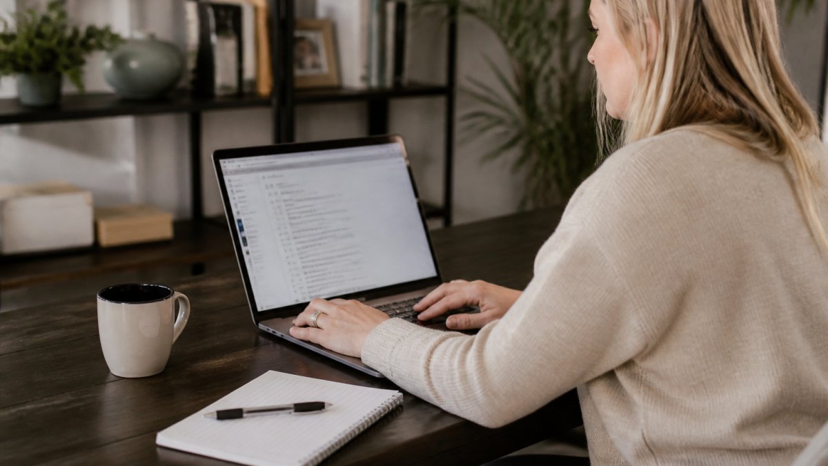 Sales professional at desk reviewing automated email sequences on laptop screen with notepad and coffee cup nearby