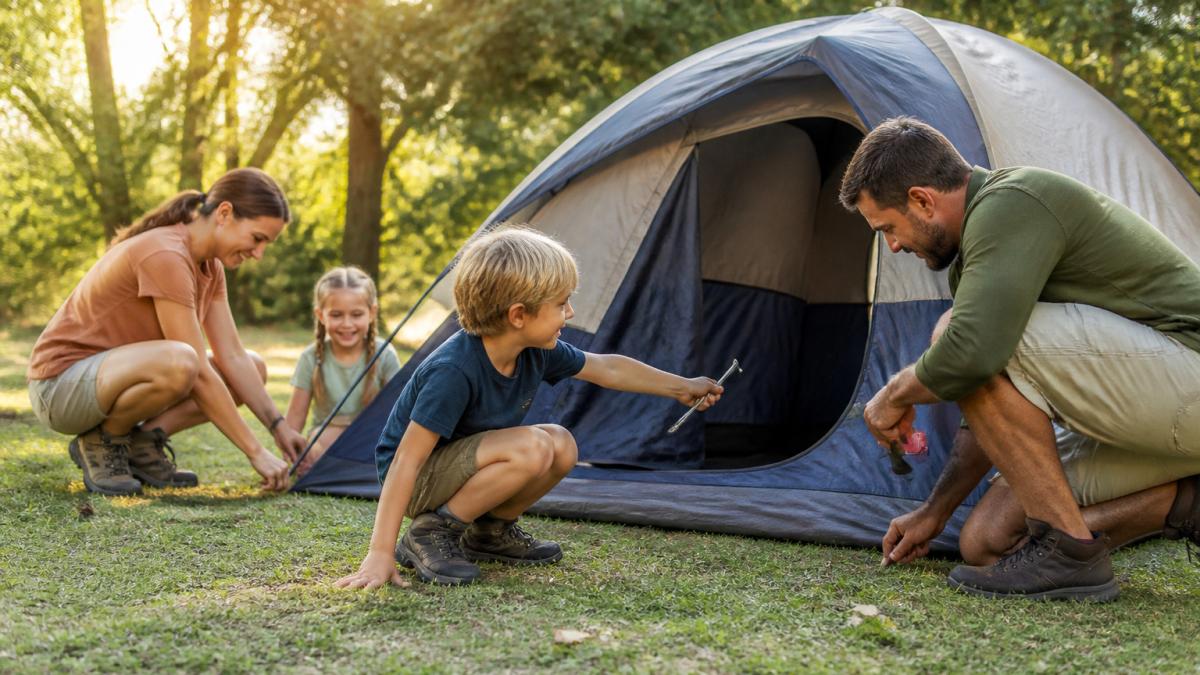A family of four working together to pitch a dome tent on a grassy campsite during golden hour.