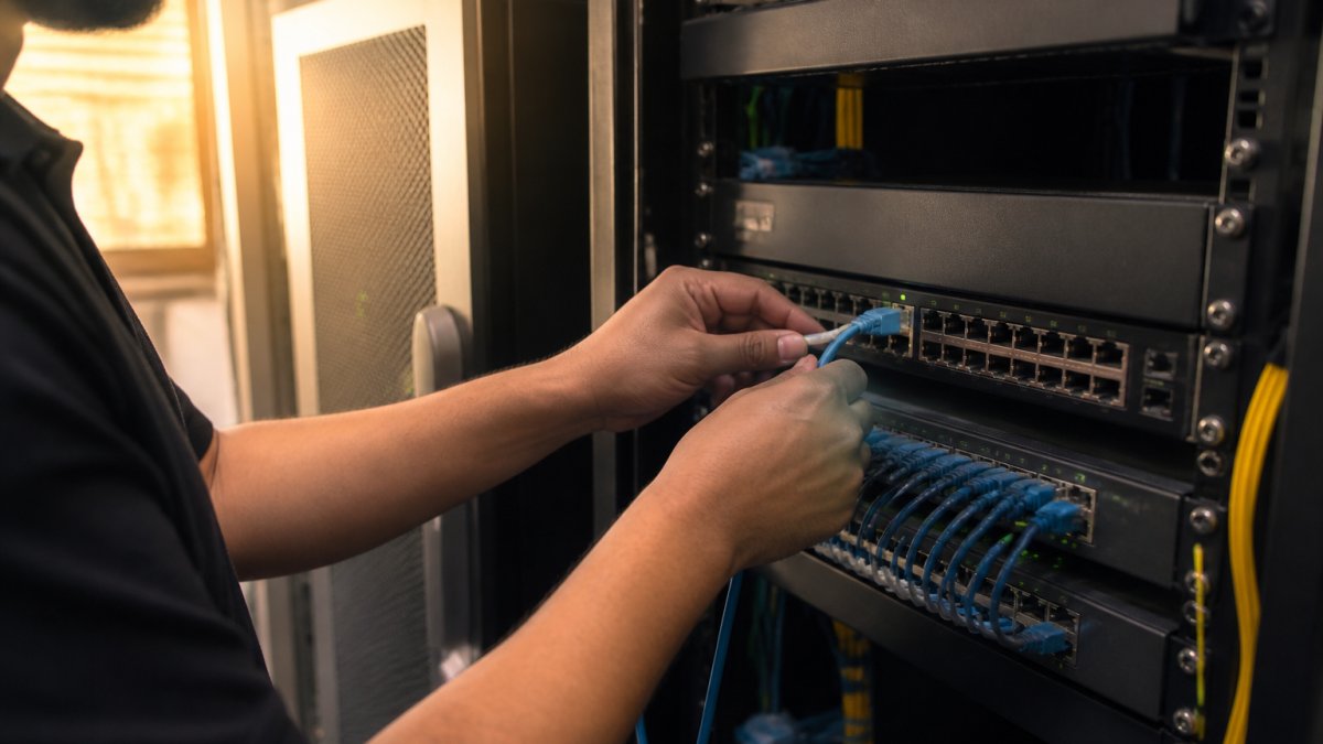 Hotel IT professional monitoring network segmentation dashboards on multiple screens in server room, with network diagrams displayed, professional lighting