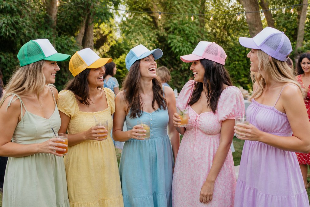 Bridesmaids in pastel dresses wearing trucker hats at a sustainable bridal party garden celebration