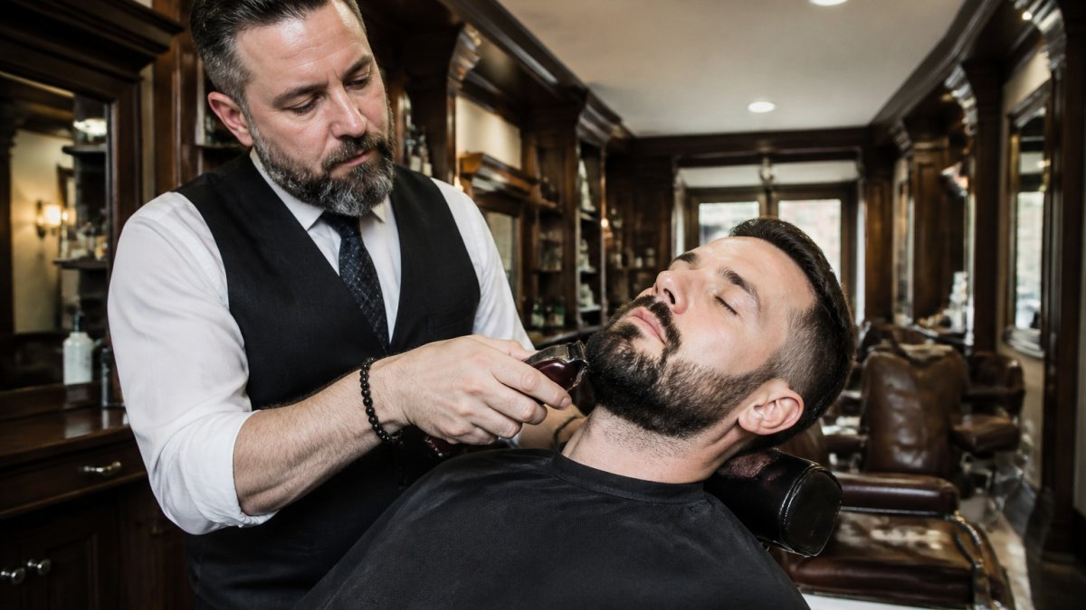 Barber using precision clippers for a beard trim in a Maryland barbershop offering men's grooming services.