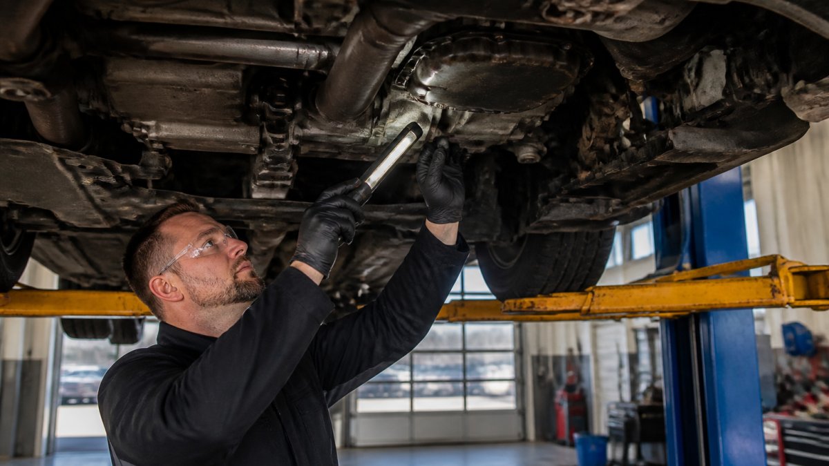 Mechanic inspecting a failing truck torque converter under a GMC vehicle in a repair shop