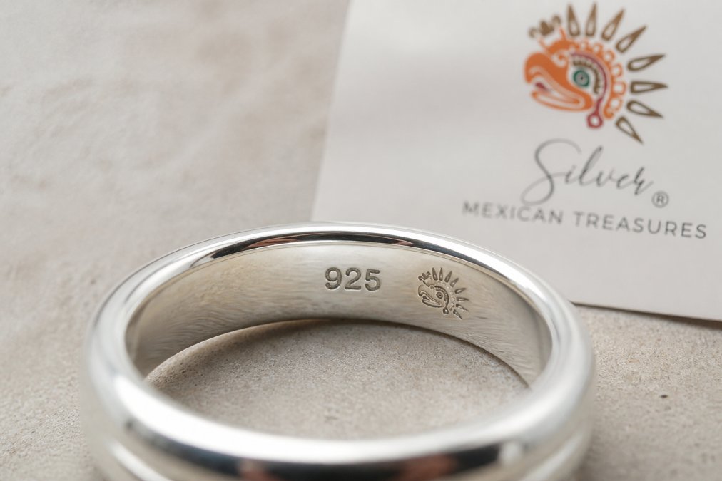 Close-up of a polished sterling silver ring showing a clear 925 hallmark stamp etched into the band, with maker's mark visible beside it under bright studio lighting