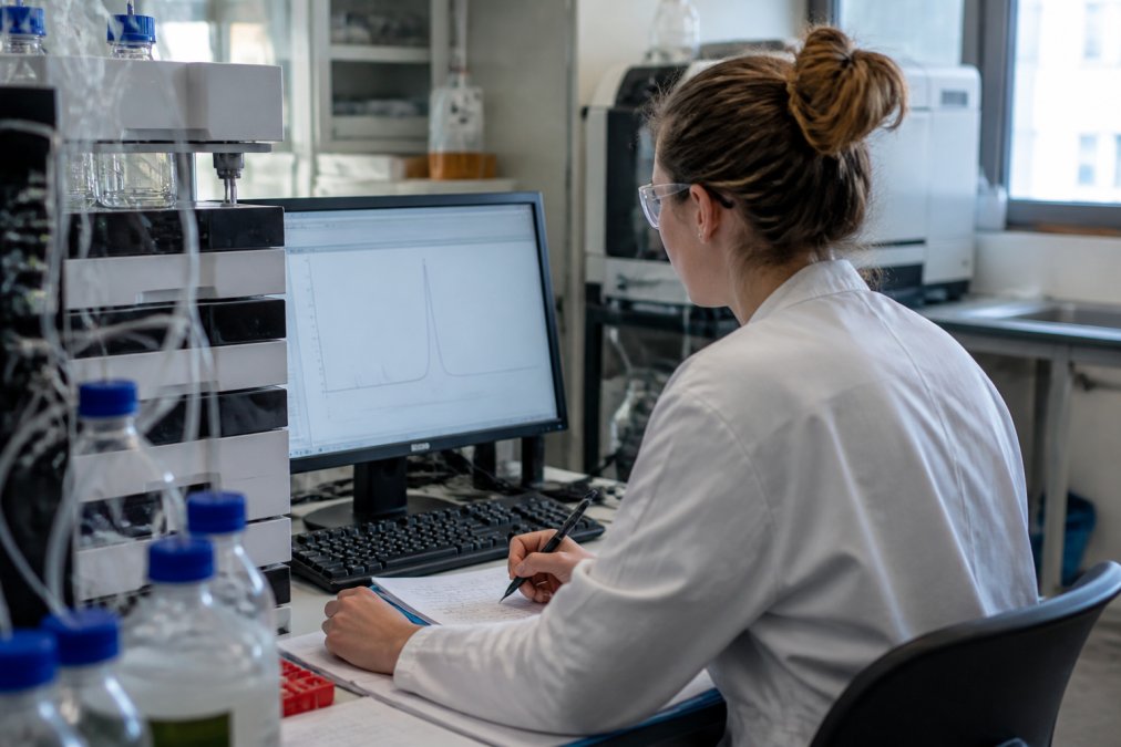 Laboratoriumtechnicus analyseert HPLC-chromatogrammen op een computermonitor in een modern onderzoekslaboratorium, omringd door apparatuur en notities