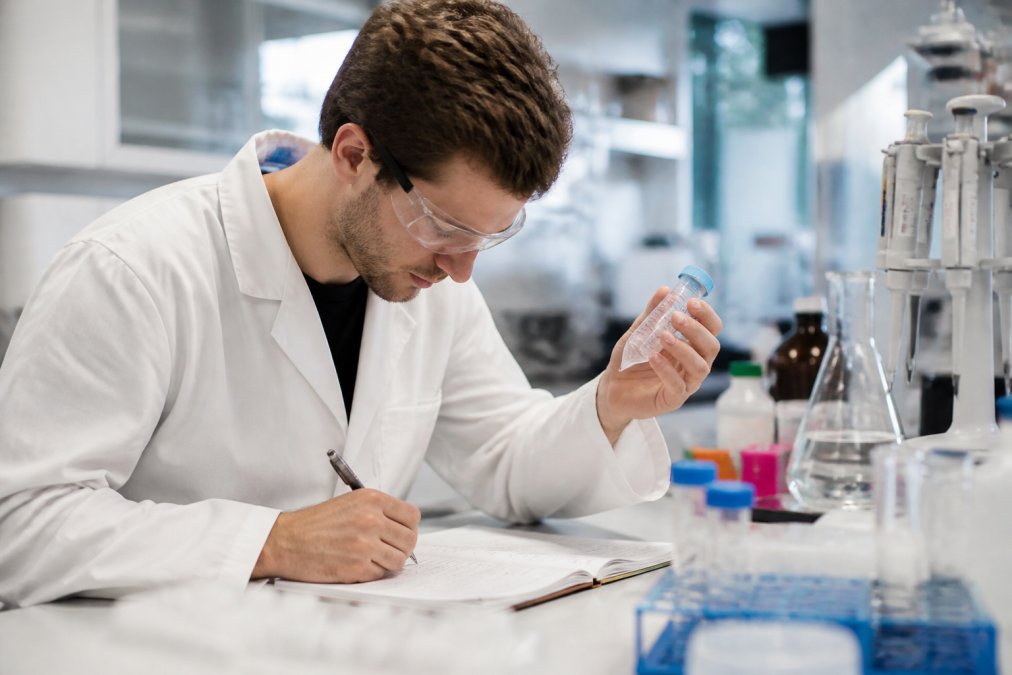 Onderzoeker voert peptide-experimenten uit met testbuizen en laboratoriumapparatuur, terwijl hij gegevens in een notitieboek registreert