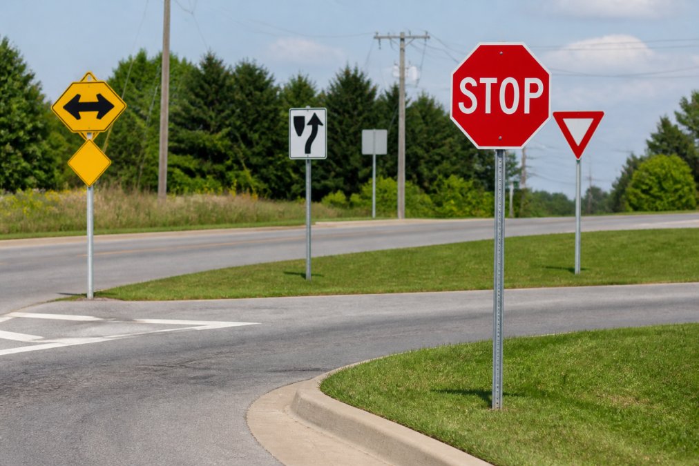 Street intersection showing multiple traffic signs including stop sign, yield sign, and directional signs mounted on poles with clear visibility and proper spacing