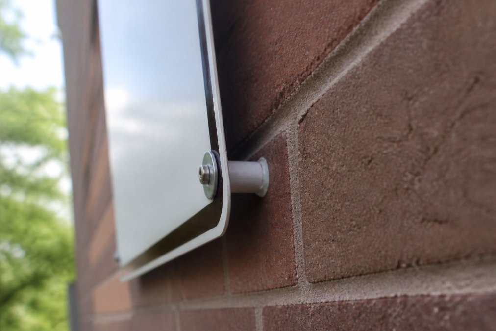 Close-up of a metal aluminum sign mounted on a brick wall with visible mounting hardware and anchors, showing proper installation technique and weatherproofing