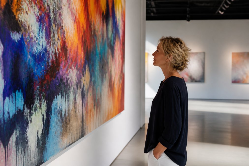 Person standing before a vibrant abstract painting in a contemporary gallery space, body relaxed, gazing thoughtfully at the canvas with soft natural light illuminating their face