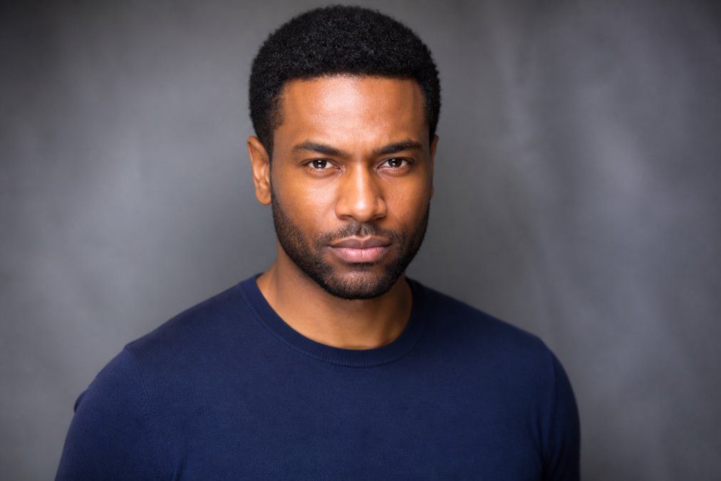 Actor in professional solid-color fitted top photographed from shoulders up against neutral studio background with professional lighting, showing confident expression and authentic presence