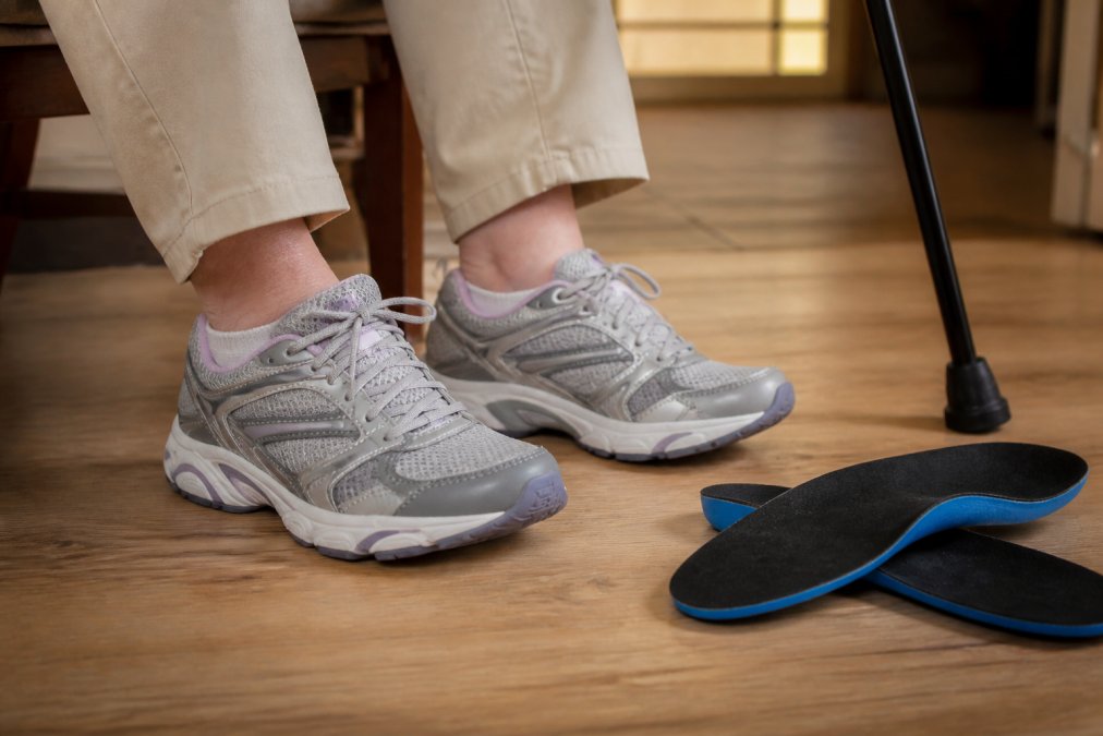 Person wearing wide-fit sneakers with arch support insoles as essential mobility gear near a walking stick