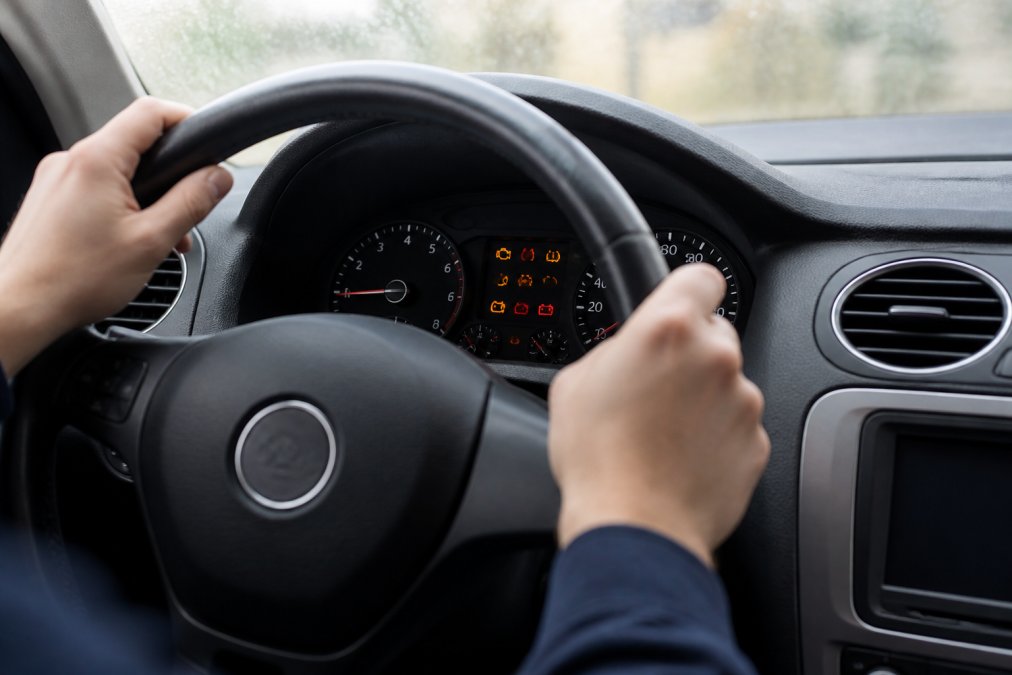 Vehicle dashboard displaying illuminated ADAS warning lights and system alerts, with the driver's hands visible on the steering wheel showing concern