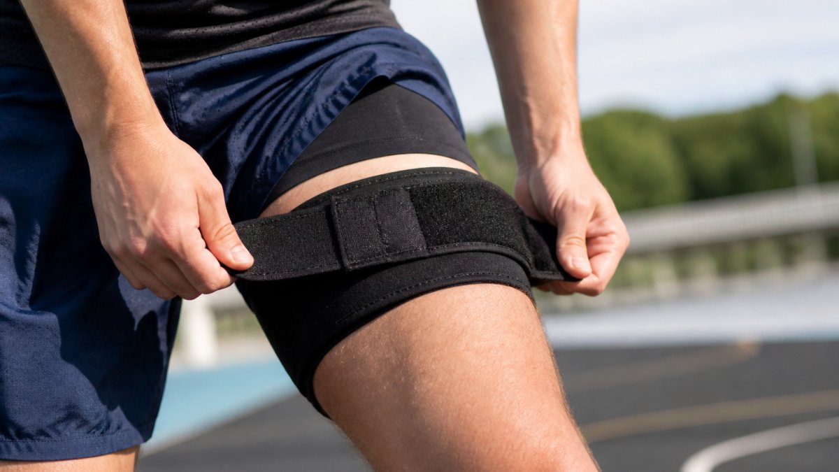 Close-up of hands positioning an adjustable thigh wrap around the upper leg, showing proper strap alignment and compression placement during athletic setup in natural daylight
