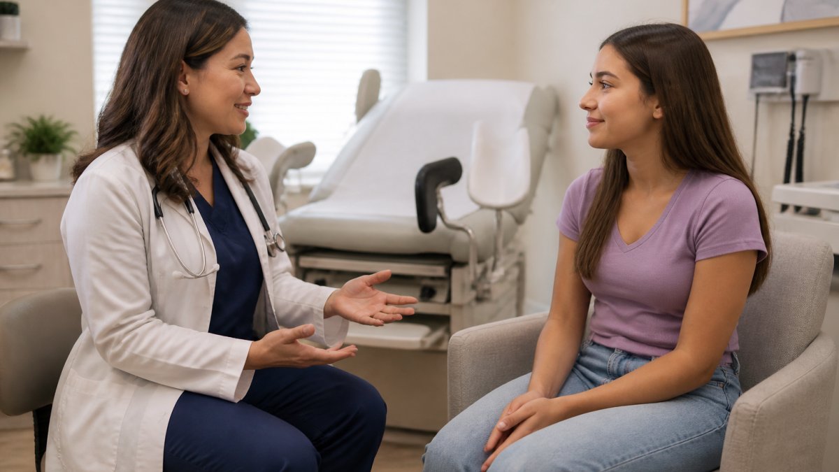Healthcare provider in clinical office speaking with teenage girl in comfortable seating, both relaxed and engaged in conversation, warm lighting creating welcoming atmosphere