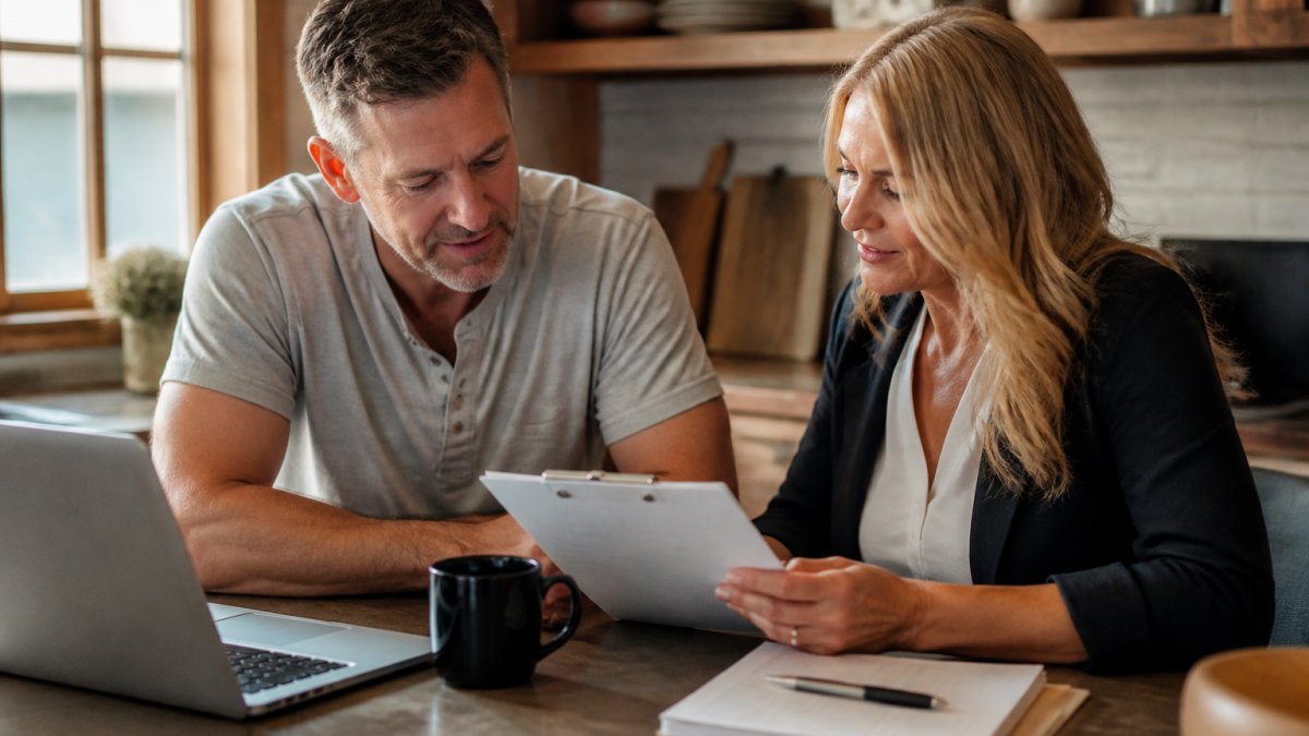 Professional financial advisor and client reviewing estate planning documents together at a desk with laptop and notebook visible, natural office lighting