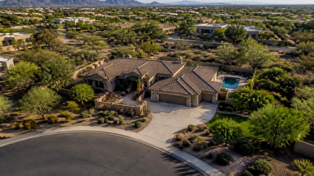 Professional drone camera capturing aerial view of residential property showing complete home footprint, yard, driveway, and neighboring landscape from above with clear skies