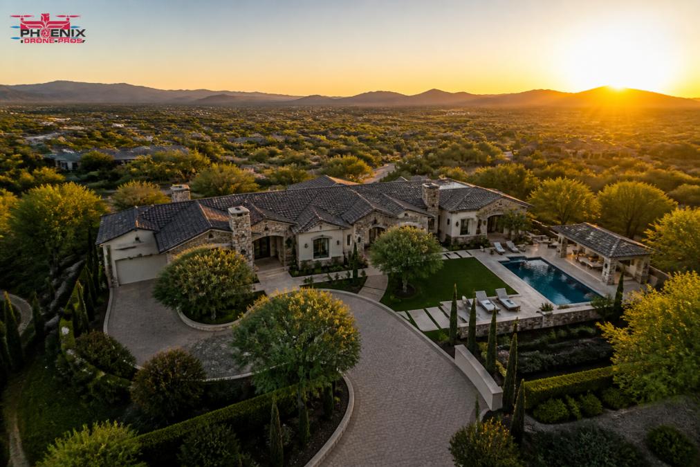Drone ascending over a luxury estate with manicured gardens and pool visible below during golden hour, showing cinematic perspective and property boundaries