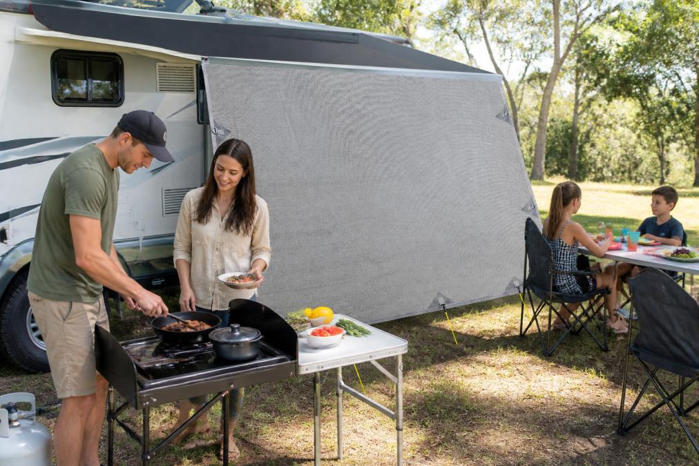Family preparing a meal outdoors at a caravan campsite with cast iron cookware and portable stove, children sitting at a folding camping table nearby