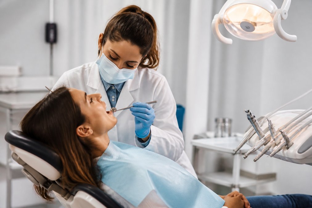 Patient sitting in a modern dental chair during a routine examination with a dental professional using professional equipment and instruments in a bright, clinical setting