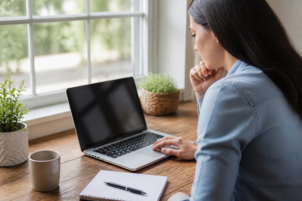 Person using a laptop to research dental clinics and book an appointment, with a notepad and pen nearby for taking notes on a home desk with natural window lighting